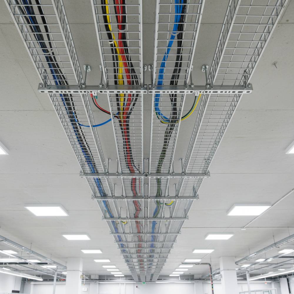 Instalação de eletrocalhas aramadas inox em teto de fábrica, com cabos elétricos sendo roteados de forma organizada.